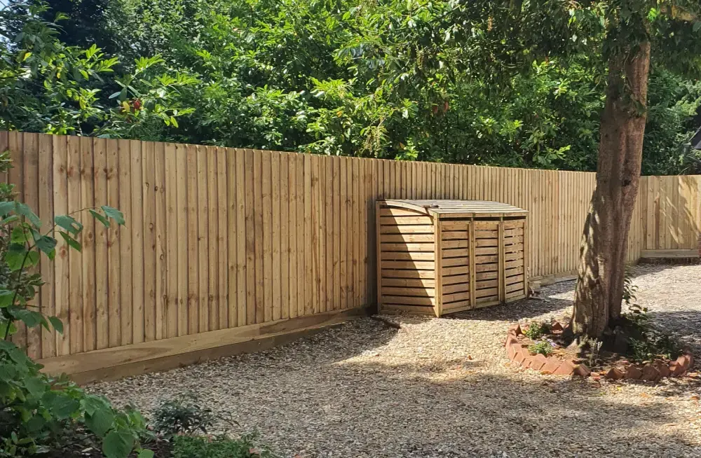 A long run of new closeboard featheredge fencing on gravel boards, running behind a gravel path and a timber bin store