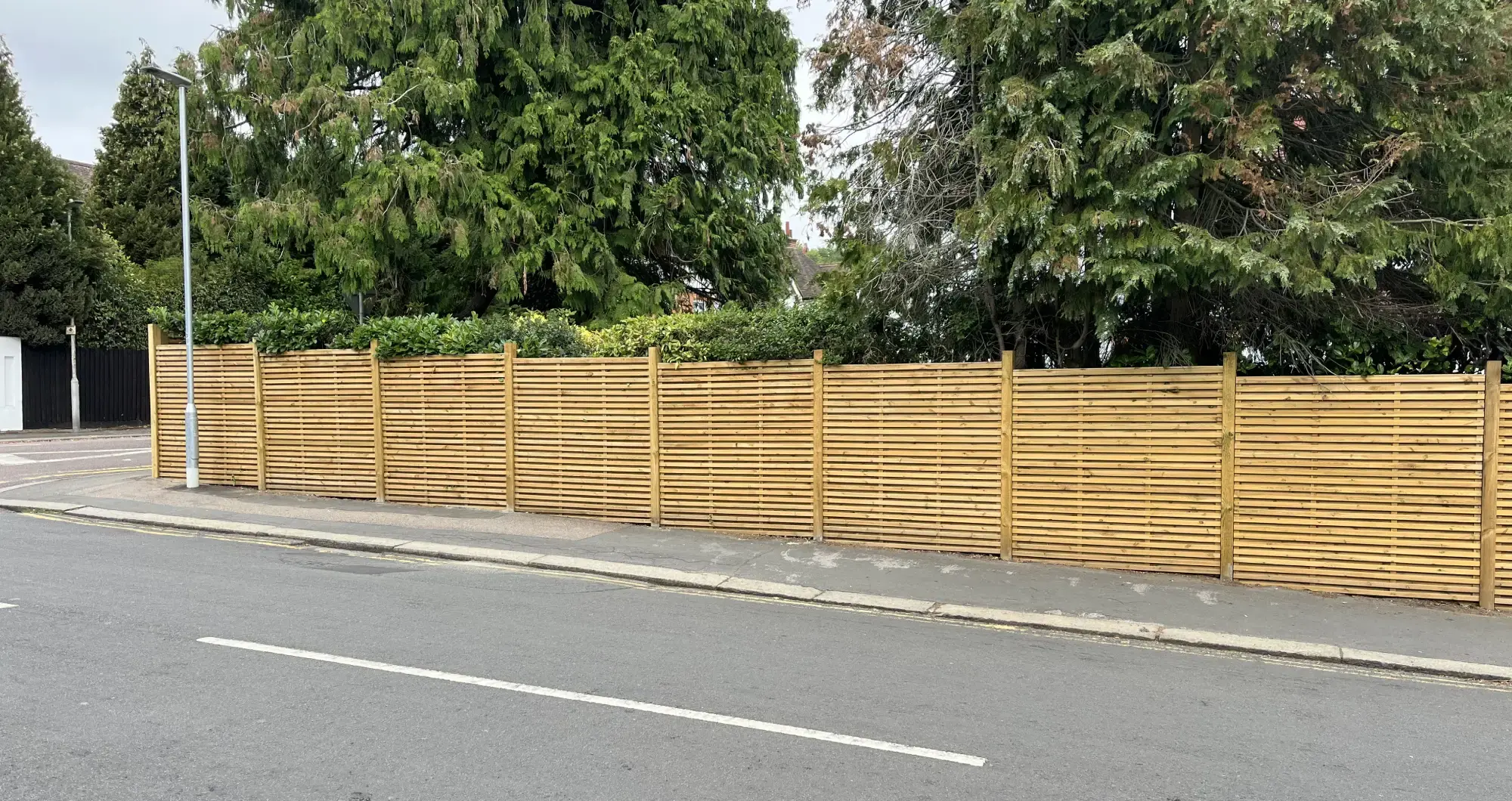 A long run of slatted screen fencing stepping down a pavement in Beaconsfield